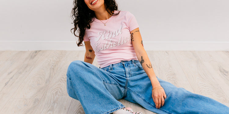 Woman wearing a pink t-shirt and blue jeans sitting on a light-colored floor.