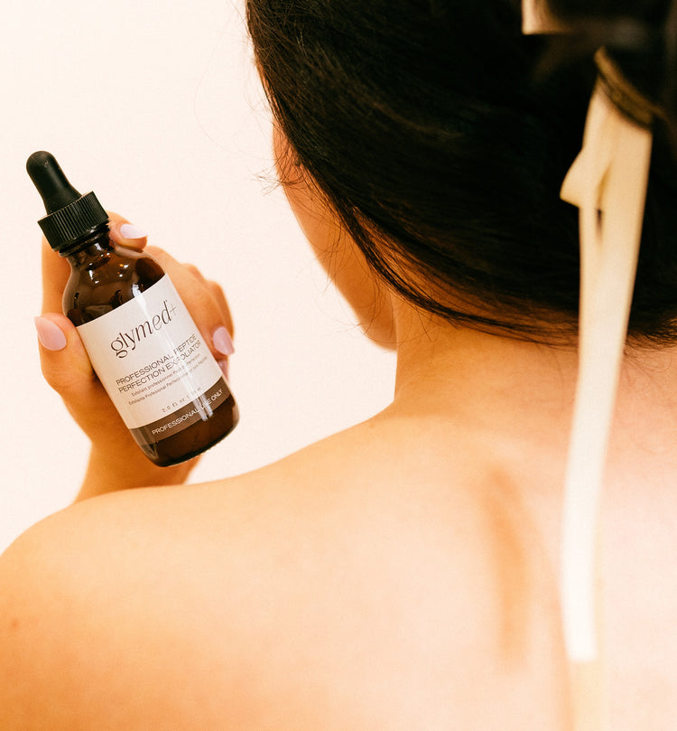 Women with her back facing the camera holding a glymed skincare product.